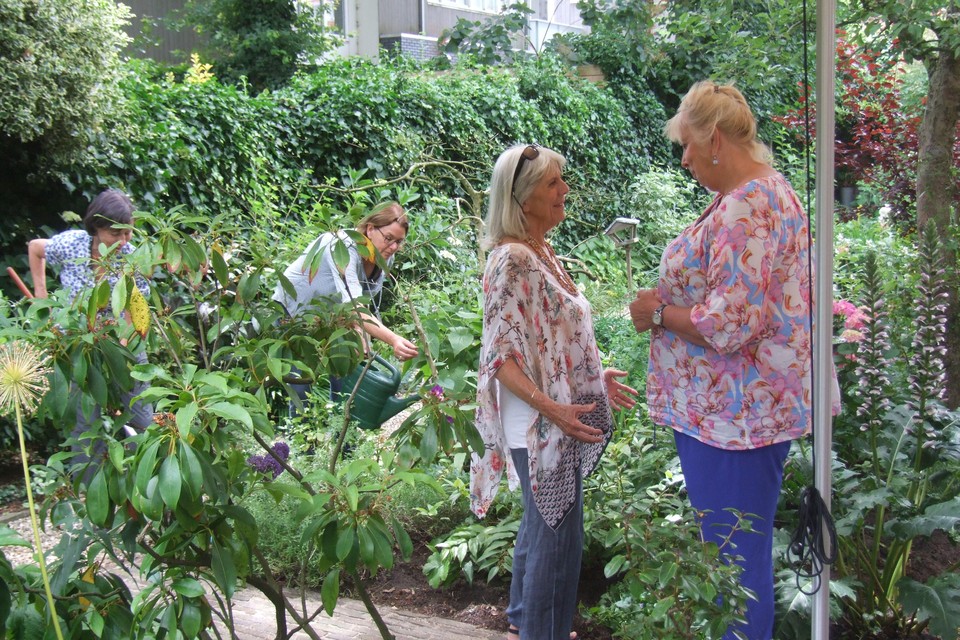 Erna Gianotten (links) praat met Christien de Groot in de hospice-tuin. Op de achtergrond tuinvrijwilligers.