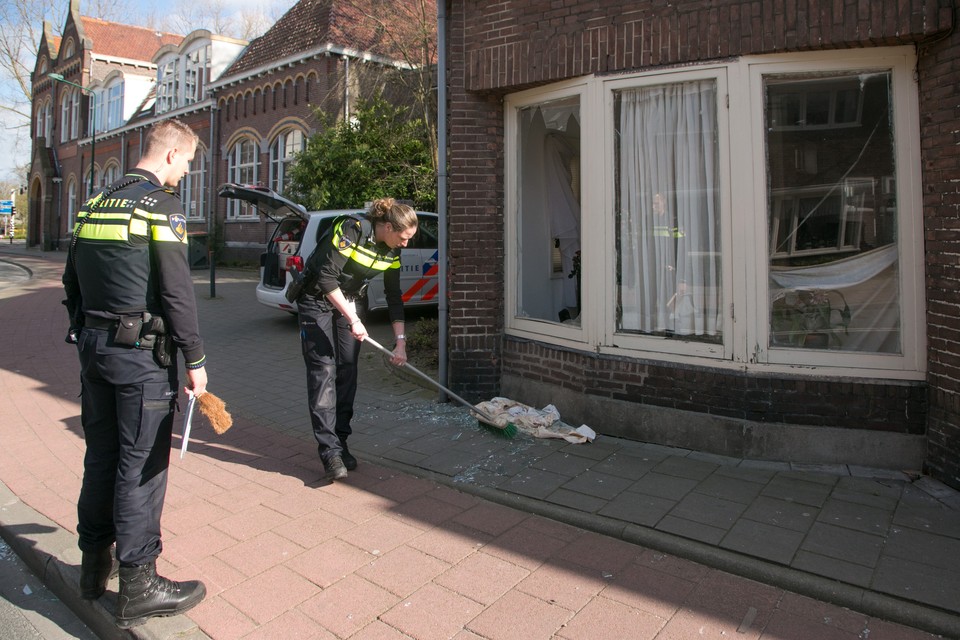 Politieagenten vegen glas bij het getroffen huis. Foto Caspar Huurdeman