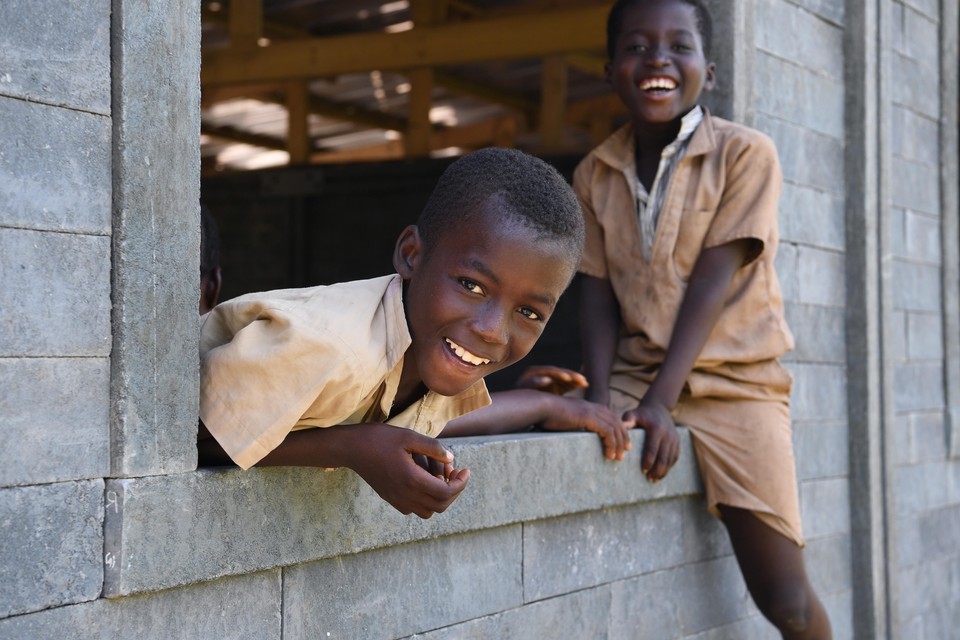 Blije kinderen hanfgen uit de vensters van hun plastic klaslokaal in het dorp Sakassou in de Ivoorkust.