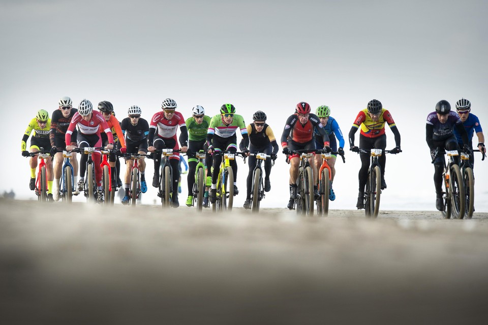Michel Butter, in het midden met startnummer 86 en in een geel-zwart trico met zwart armsleeves, rijdt tussen de collega-mountainbikers op het strand.