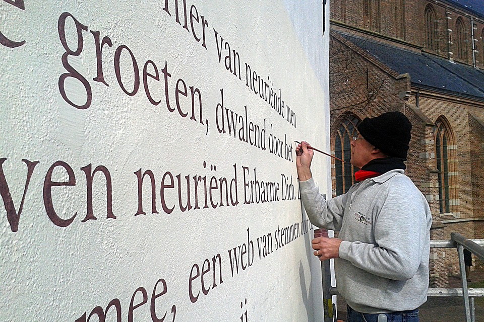 Jeroen Paulussen, hier aan het werk in Naarden in 2013, schildert ook de gedichten op de gevels in het centrum van Bussum. Foto: Familie Paulussen