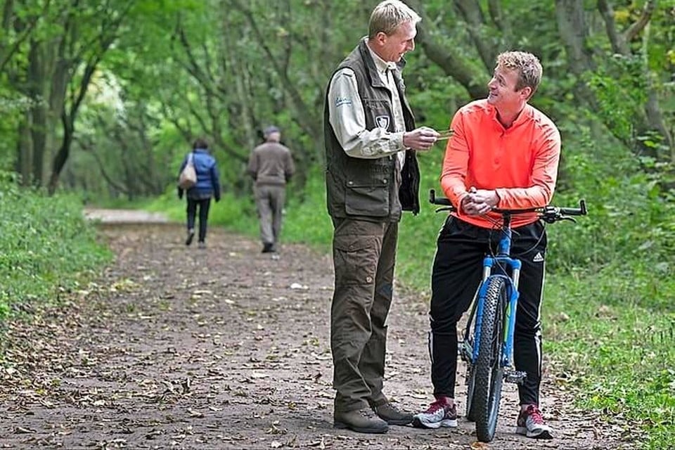 Een boswachter controleert of een fietser een duinkaart heeft.