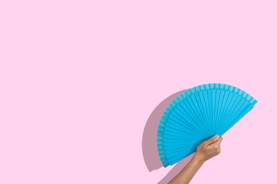 Cropped Woman Hand Holding A Blue Folding Fan Over Pink Background