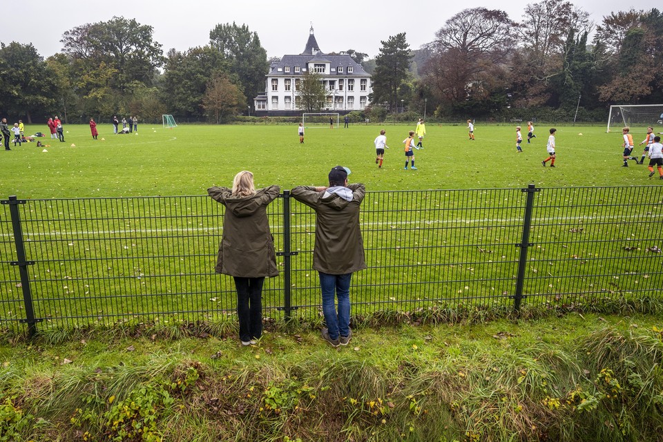 Ouders kijken van achter het hek bij Koninklijke HFC naar de verrichtingen van hun zoon.