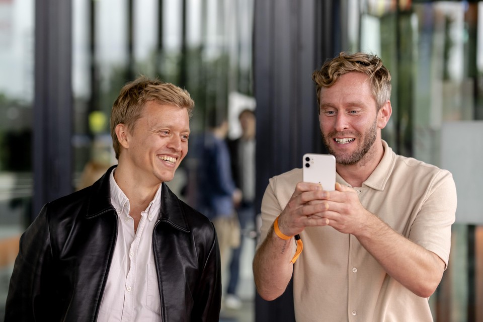 Nicolaas Veul en Tim den Besten bekijken een bericht op een mobieltje tijdens de seizoenspresentatie van de NPO.