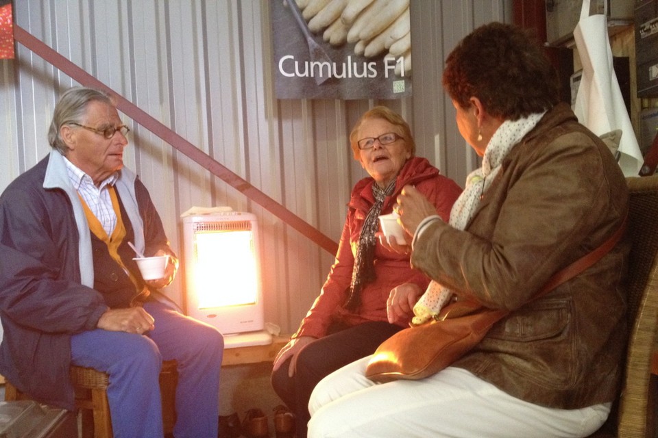 'Aspergemoeder' Maria Heger (77) met haar klanten Petronella en Jan van Seumeren bij het straalkacheltje in de aspergeloods.