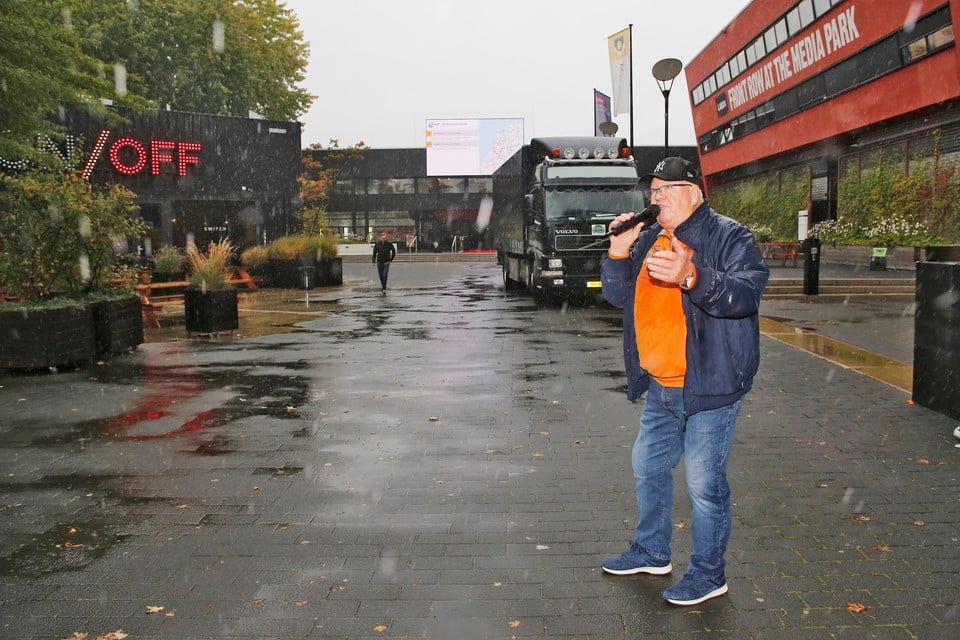 Henk Wijngaard geeft er in de regen op het Mediapark luid zingend van langs.
