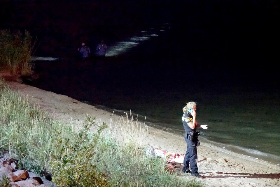 Een agent op strand, bij de achtergelaten spullen van de verdwenen jonge vrouw uit Alkmaar. Achter haar wordt gezocht in het Markermeer.